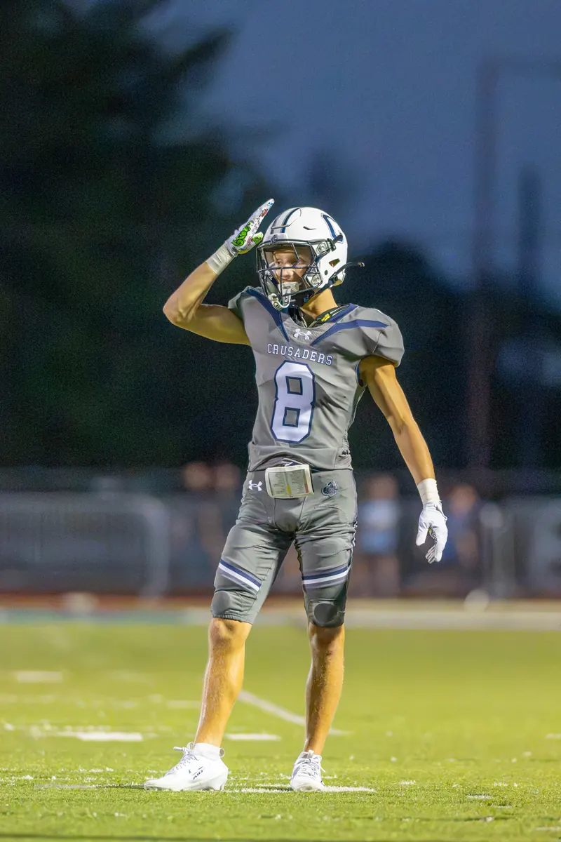 A football wide receiver in a gray uniform salutes the sideline on the field at dusk