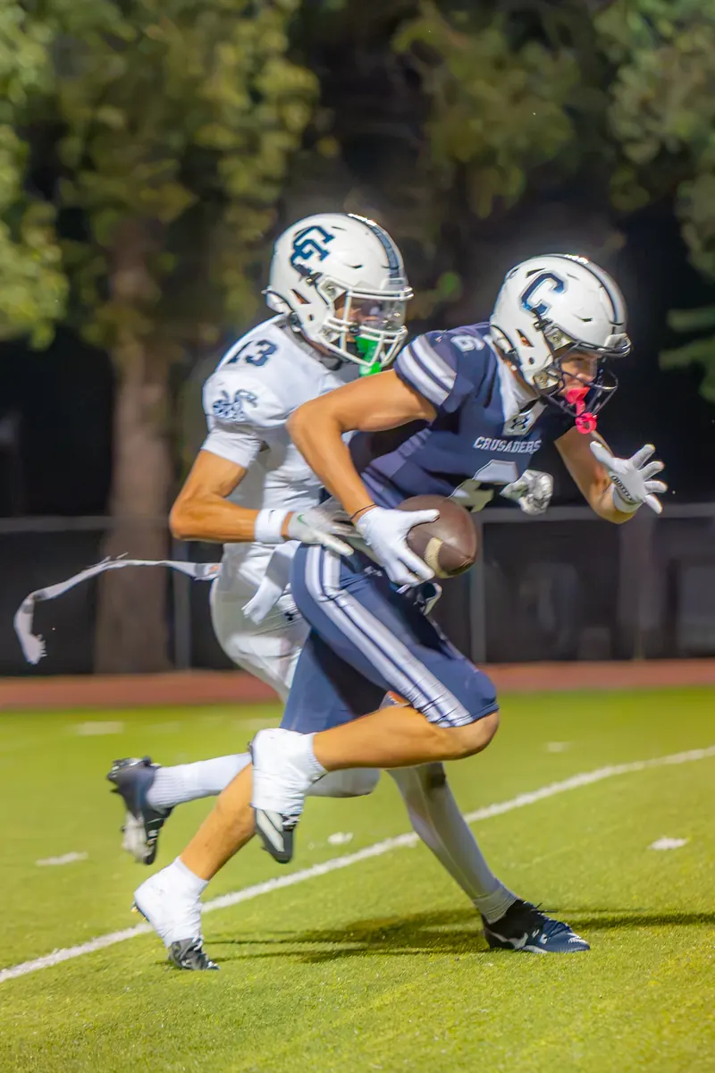 A football ball carrier in a navy jersey sprints past a defender under the stadium lights